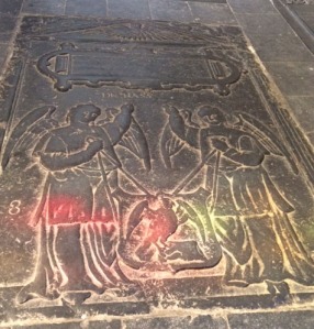 A grave slab with angels, tinted by the light through stained glass.
